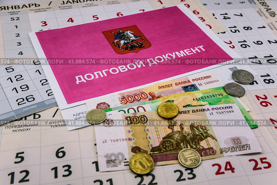 Долговой документ за неуплату жилищно-коммунальных услуг (ЖКУ), российские деньги-банкноты и монеты лежат на листках календаря. Стоковое фото, фотограф Владимир Устенко / Фотобанк Лори