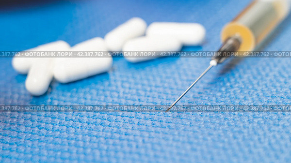 Doping in tablets and syringe on blue background next to dumbbells, concept of use of prohibited drugs in sports, oral and intramuscular medications. Стоковое фото, фотограф Скрипачев Антон / Фотобанк Лори