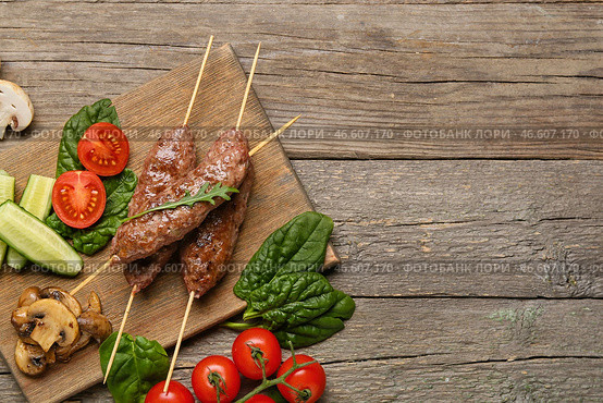 Доска для шашлыка с вкусным люля-кебабом и овощами на деревянном фоне. Стоковое фото, фотограф Pixel_shot / Фотобанк Лори