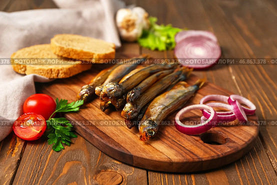 Доска с вкусной копченой мойвой на деревянном фоне, крупным планом. Стоковое фото, фотограф Pixel_shot / Фотобанк Лори