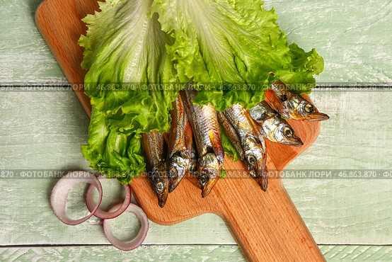 Доска с вкусной копченой мойвой, завернутой в листья салата, на зеленом деревянном фоне. Стоковое фото, фотограф Pixel_shot / Фотобанк Лори