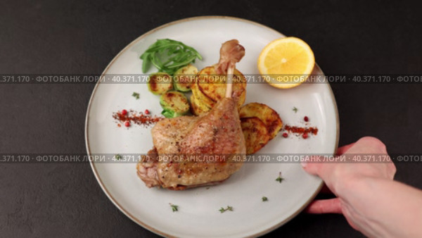 Duck leg confit with Brussels sprouts, baked potatoes, thyme, orange and lingonberry sauce. Traditional French cuisine. Woman puts a plate on the table. Selective focus, close-up, black background. Стоковое видео, видеограф Наталья Любина / Фотобанк Лори