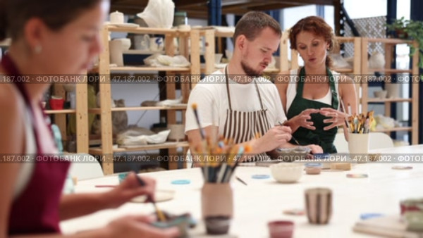 During master class, student paints clay vessel under guidance of female teacher. Стоковое видео, видеограф Яков Филимонов / Фотобанк Лори