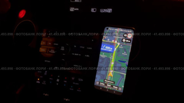 Движение легкового автомобиля в темное время суток. Вид на переднюю панель автомобиля с закрепленным смартфоном, открыта навигационная программа. Свет от фонарей на улице периодически освещает салон. Свет и тени (2023 год). Стоковое видео, видеограф Щеголева Ольга / Фотобанк Лори