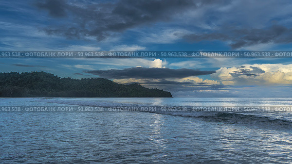 Early morning. The ocean waves are foaming and spreading across the beach. The clouds in the blue sky are illuminated with golden light. A hill in the distance. Malaysia. Borneo. Kota Kinabalu. Стоковое фото, фотограф Вера Ивановна Кубарева / Фотобанк Лори