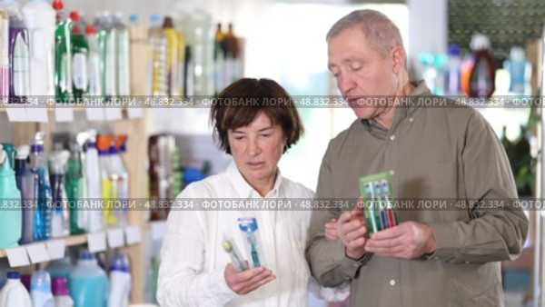 Elderly couple choosing toothbrushes and mint paste in the department with household chemicals in the supermarket. Стоковое видео, видеограф Яков Филимонов / Фотобанк Лори
