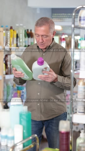 Elderly European man in the household section of a supermarket holds rinses and fabric softeners. Buyer chooses a liquid laundry detergent. Стоковое видео, видеограф Яков Филимонов / Фотобанк Лори