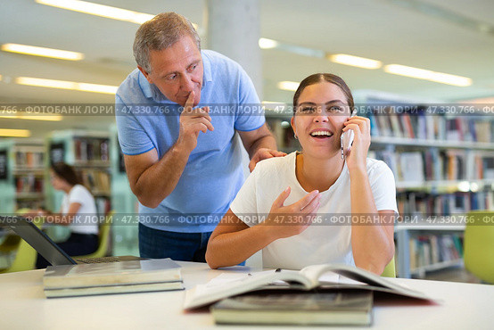 Elderly librarian asks young woman who is talking loudly on mobile phone to keep quiet. Стоковое фото, фотограф Яков Филимонов / Фотобанк Лори
