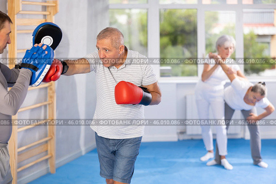Elderly man hitting focus mitts held by his boxing trainer. Стоковое фото, фотограф Яков Филимонов / Фотобанк Лори