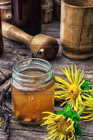 Elecampane tincture. infusion of inflorescences and roots of the medicinal plant Inula on the wooden table next mortar and pestle.Photo tinted.Selective focus. Стоковое фото, агентство Ingram Publishing / Фотобанк Лори