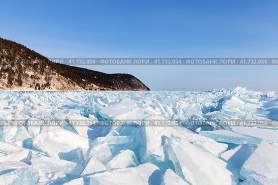 Endless hummock fields with piles of huge transparent blue ice floes at the shore of frozen Baikal Lake near village of Goloustnoye on frosty sunny January day. Beautiful winter landscape. Natural background. Стоковое фото, фотограф Виктория Катьянова / Фотобанк Лори