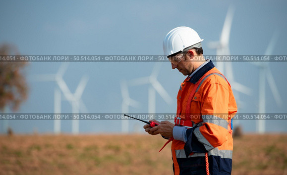 Engineer at Natural Energy Wind Turbine site with a mission to take care of large wind turbines Use a walkie talkie to communicate with a colleague working on top of the wind turbine. Стоковое фото, агентство Ingram Publishing / Фотобанк Лори