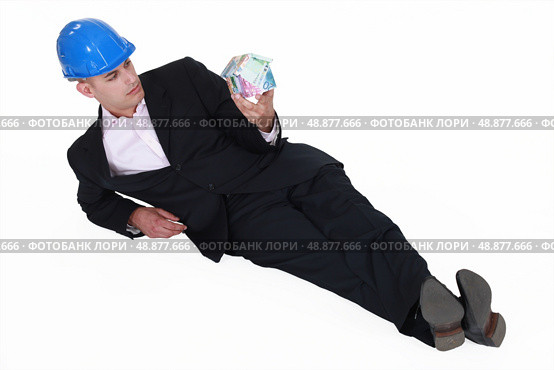 Engineer lazily lying on the floor and staring at a house made of money. Стоковое фото, агентство Ingram Publishing / Фотобанк Лори