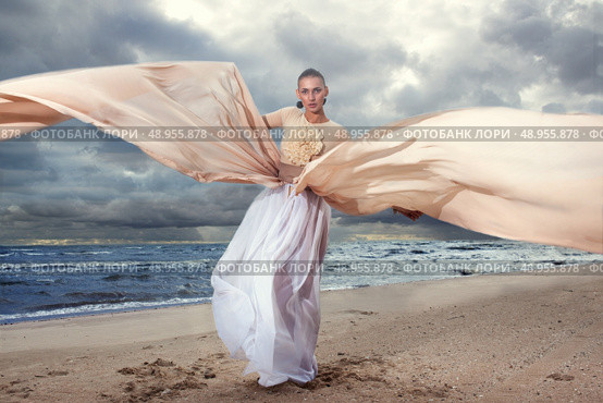 Fashionable model posing in extremely long dress on the seashore. Стоковое фото, агентство Ingram Publishing / Фотобанк Лори