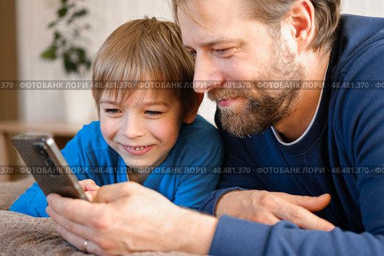 Father and son little boy laughing and using phone. They watching funny videos together, playing games on smartphone. Concept technology, smart phone addicted. Fun weekend activity. Modern fatherhood. Стоковое фото, фотограф Марина Демидюк / Фотобанк Лори