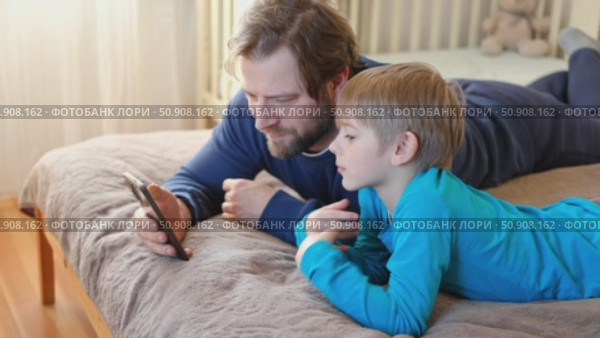 Father and son little boy laughing and using phone. They watching funny videos together, playing games on smartphone. Concept technology, smartphone addicted. Fun weekend activity. Modern fatherhood. Стоковое видео, видеограф Марина Демидюк / Фотобанк Лори
