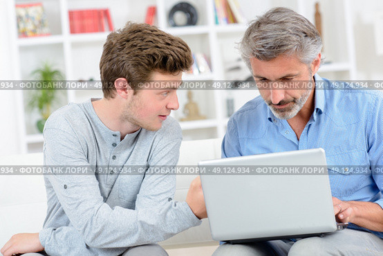 Father using laptop, teenage son next to him. Стоковое фото, агентство Ingram Publishing / Фотобанк Лори