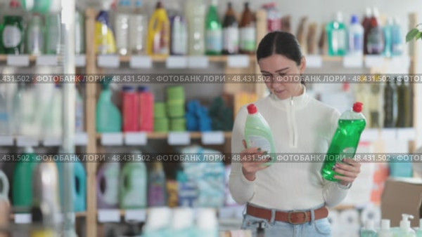 Female customer stands in the household section of a supermarket and chooses between a regular and eco-friendly dishwashing detergent. Woman shopping for household products for the home. Стоковое видео, видеограф Яков Филимонов / Фотобанк Лори