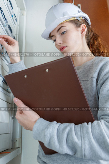 Female electrician at fusebox holding clipboard. Стоковое фото, агентство Ingram Publishing / Фотобанк Лори