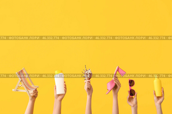 Female hands with miniature deck chair, seashell, sunscreens, sunglasses and heeled sandal on yellow background. Travel concept. Стоковое фото, фотограф Pixel_shot / Фотобанк Лори