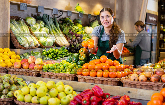 Female seller holding mandarin oranges standing in fruit and vegetable section of supermarket. Стоковое фото, фотограф Яков Филимонов / Фотобанк Лори