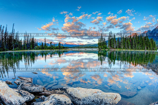 First glimpse of golden sunrise at Pyramid Lake in Jasper National Park, Alberta, Canada. The clouds reflect off the calm waters. Стоковое фото, агентство Ingram Publishing / Фотобанк Лори