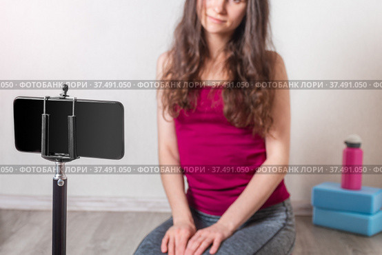 Fitness young woman sitting on the floor and looking at mobile phone. Yoga blocks and water bottle are in the background. Close-up. Selective focus. Стоковое фото, фотограф Алдошина Екатерина / Фотобанк Лори