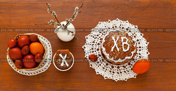 Flat lay of Easter composition with homemade Easter cake on lace handmade napkin, pussy willow branches and painted red Easter eggs on wooden table. On Easter cake letters ХВ mean Christ is Risen. Стоковое фото, фотограф Виктория Катьянова / Фотобанк Лори