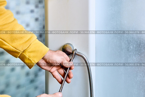 Flexible shower hose connection process shows installer tightening hose onto shower mixer outlet using open-end wrench with clear detail of threading at attachment point. Стоковое фото, фотограф Владимир Григорьев / Фотобанк Лори