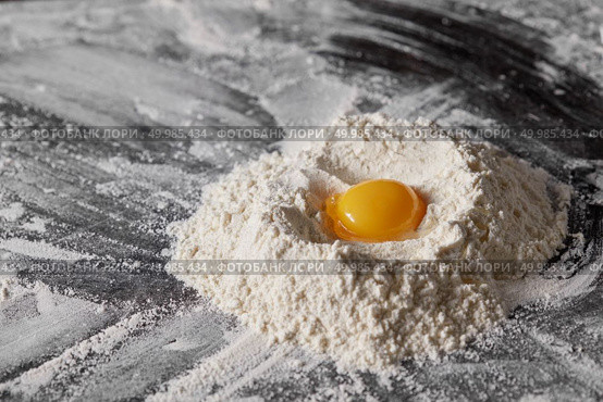 Flour and raw egg on the kitchen table, ingredients for kneading the dough. Pile of flour and egg on the kitchen table. Стоковое фото, агентство Ingram Publishing / Фотобанк Лори