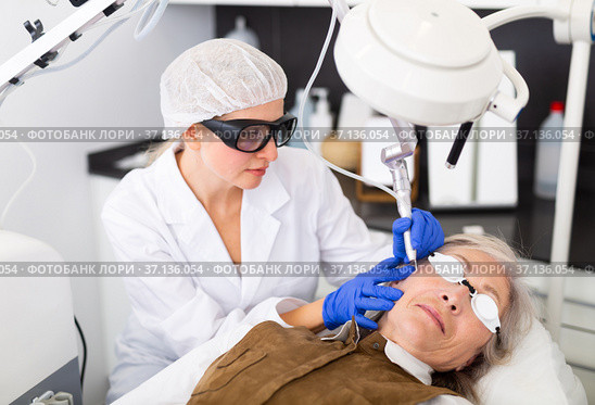Focused cosmetologist performing laser resurfacing to senior woman. Стоковое фото, фотограф Яков Филимонов / Фотобанк Лори