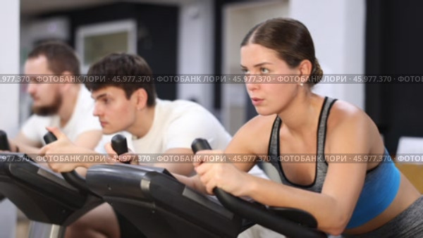 Focused girl works out with stationary bicycle during class at fitness club. Стоковое видео, видеограф Яков Филимонов / Фотобанк Лори