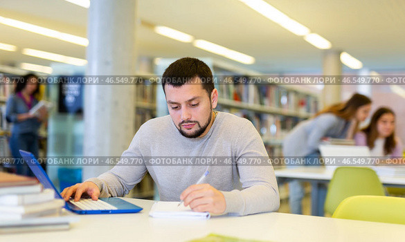 Focused guy student studies in the library on a laptop. Стоковое фото, фотограф Яков Филимонов / Фотобанк Лори