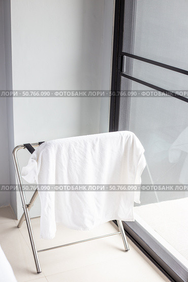 Folding drying rack with white towel in room with large window and balcony. Vertical Interior and amenities. Стоковое фото, фотограф Коханова Наталья / Фотобанк Лори