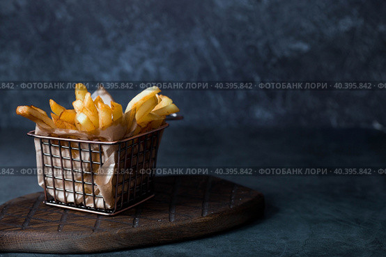 French fries in a metal basket with salt on a stylish board on a dark background. Fried potatoes. The concept of fast food and junk food. Стоковое фото, фотограф Photojuli / Фотобанк Лори