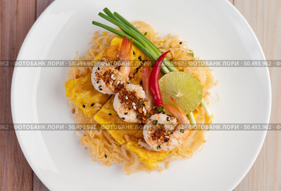 Fresh Pad Thai Shrimp with lime, lettuce, omelet and spring onions in a white plate on wooden. Стоковое фото, агентство Ingram Publishing / Фотобанк Лори