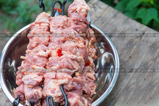 Fresh raw shish kebab in a nickel-plated bowl. Juicy pork meat is strung on skewers and placed on a rough wooden tray in the garden. Свежий сырой шашлык в никелированной миске. Сочное свиное мясо нанизывают на шампуры и выкладывают на грубый деревянный поднос в саду. Стоковое фото, фотограф Дмитрий Березнев / Фотобанк Лори