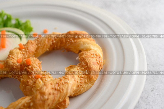 Freshly baked soft pretzel with generous sprinkling of coarse salt and sesame on white dish, decorate with lettuce and carrot beautifully, copy space. Стоковое фото, агентство Ingram Publishing / Фотобанк Лори