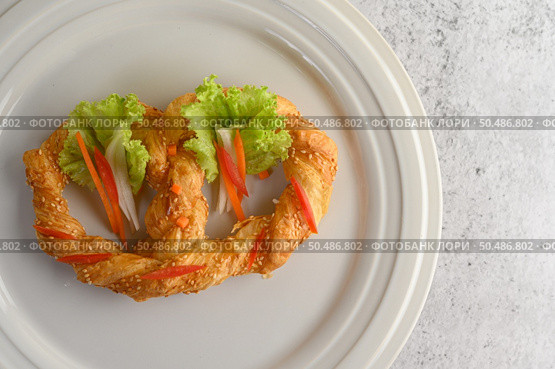 Freshly baked soft pretzel with generous sprinkling of coarse salt and sesame on white dish, decorate with lettuce and carrot beautifully, copy space. Стоковое фото, агентство Ingram Publishing / Фотобанк Лори