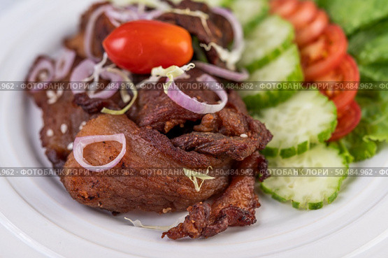 Fried pork topped with sesame, complete with tomatoes, cucumbers, cabbage, and lettuce placed in a white dish. Стоковое фото, агентство Ingram Publishing / Фотобанк Лори