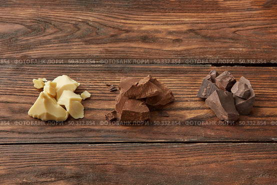 From above set of white and milk and dark chocolate crushed in chunks and placed in row on wooden table. Assortment of chocolate on wooden surface. Стоковое фото, агентство Ingram Publishing / Фотобанк Лори