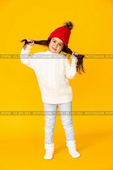 Funny child girl in a white sweatshirt and red knitted hat with pompom on a yellow background. The concept of children's emotions, joy and delight. Advertising clothing and sales. Ski resort vacation. Стоковое фото, фотограф Ирина Михайличенко / Фотобанк Лори