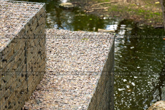 Gabion stone fence near a pond, showcasing rustic and durable landscaping with natural materials. Стоковое фото, фотограф Татьяна Степанищева / Фотобанк Лори