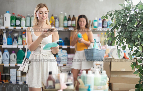 Girl buyer scans qr code on glass cleaner spray label, other client shopping in background. Стоковое фото, фотограф Яков Филимонов / Фотобанк Лори