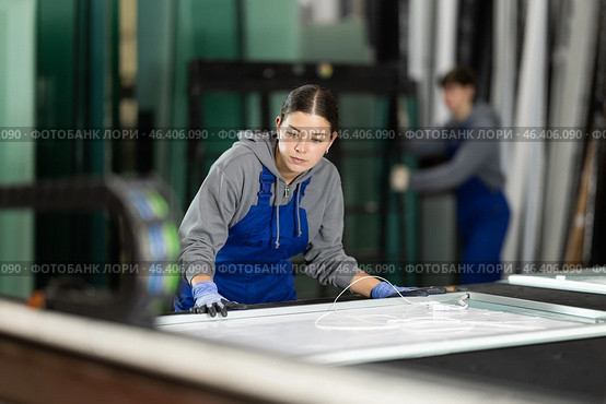 Girl glazer employee in blue overall works in glass processing shop. Стоковое фото, фотограф Яков Филимонов / Фотобанк Лори