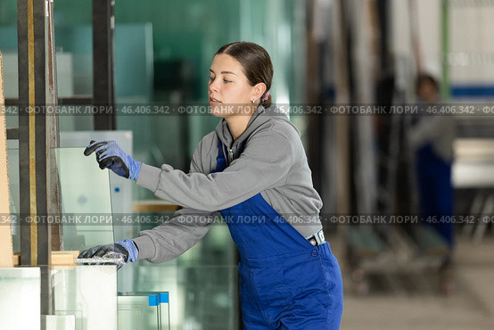 Girl glazer employee in blue overall works in glass processing shop. Стоковое фото, фотограф Яков Филимонов / Фотобанк Лори