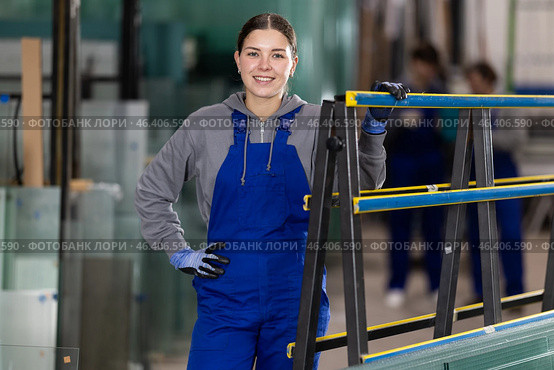 Girl glazer employee in blue overall works in glass processing shop. Стоковое фото, фотограф Яков Филимонов / Фотобанк Лори