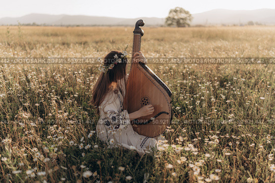Girl in folk costume and flower wreath plays bandura in field. Стоковое фото, фотограф София Тюленева / Фотобанк Лори