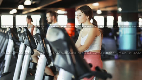 Girl performs exercises with stationary bicycle in gym. Стоковое видео, видеограф Яков Филимонов / Фотобанк Лори
