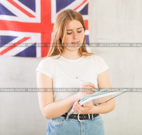 Girl student makes notes in diary.woman with notebooks stands against wall with British flag. Стоковое фото, фотограф Яков Филимонов / Фотобанк Лори
